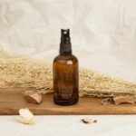 Amber glass spray bottle placed on a wooden tray with dried plants, suggesting natural cosmetics.