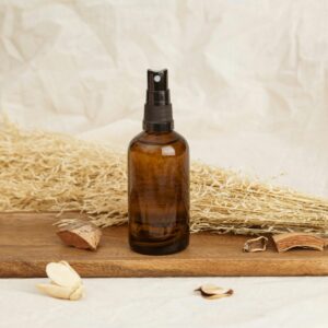 Amber glass spray bottle placed on a wooden tray with dried plants, suggesting natural cosmetics.
