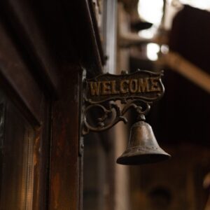 Classic vintage welcome sign with hanging brass bell in warm light.