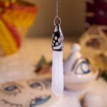 Hanging crystal pendant with intricate metalwork against a cultural background featuring symbolic designs.